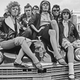 A black and white photo of young people sat on a car hood.